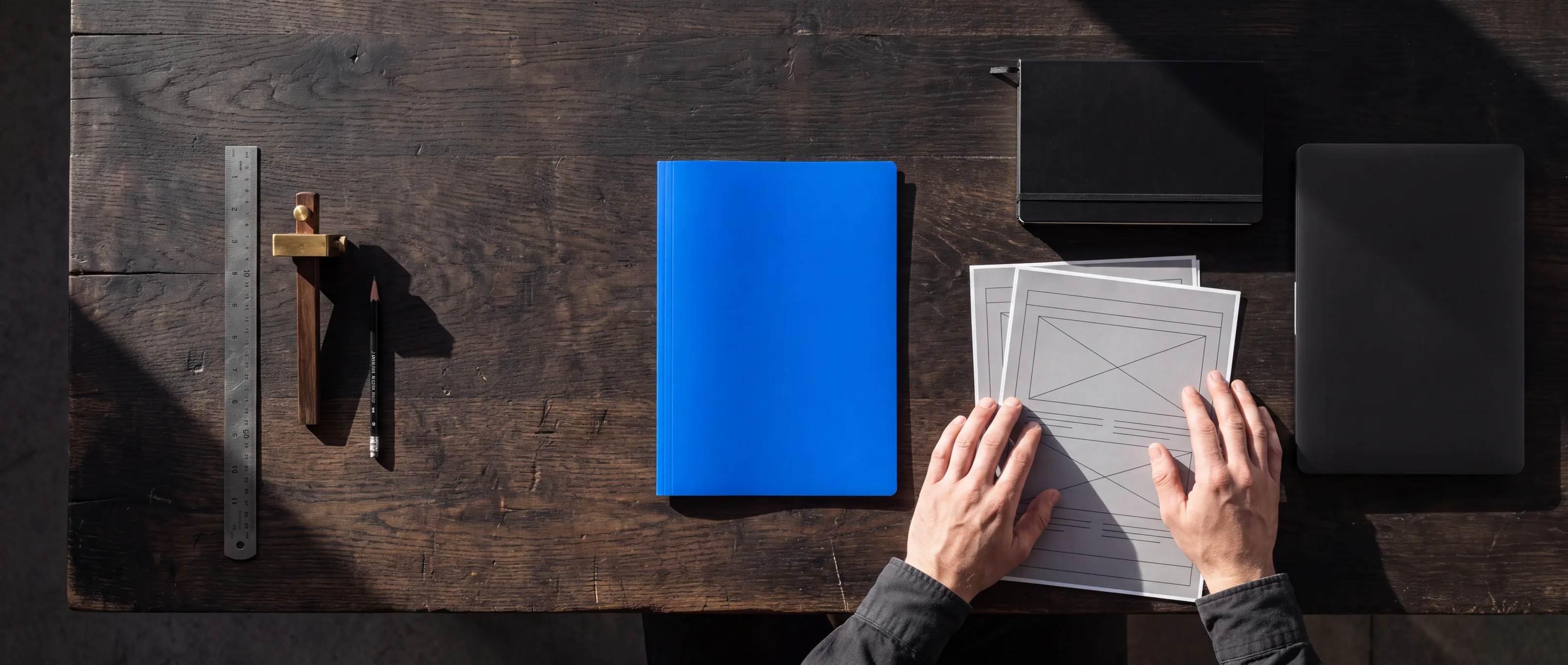 Eine Werkbank mit Werkzeug auf der einen und Wireframe-Ausdrucken, Notizbuch und Laptop auf der anderen Seite